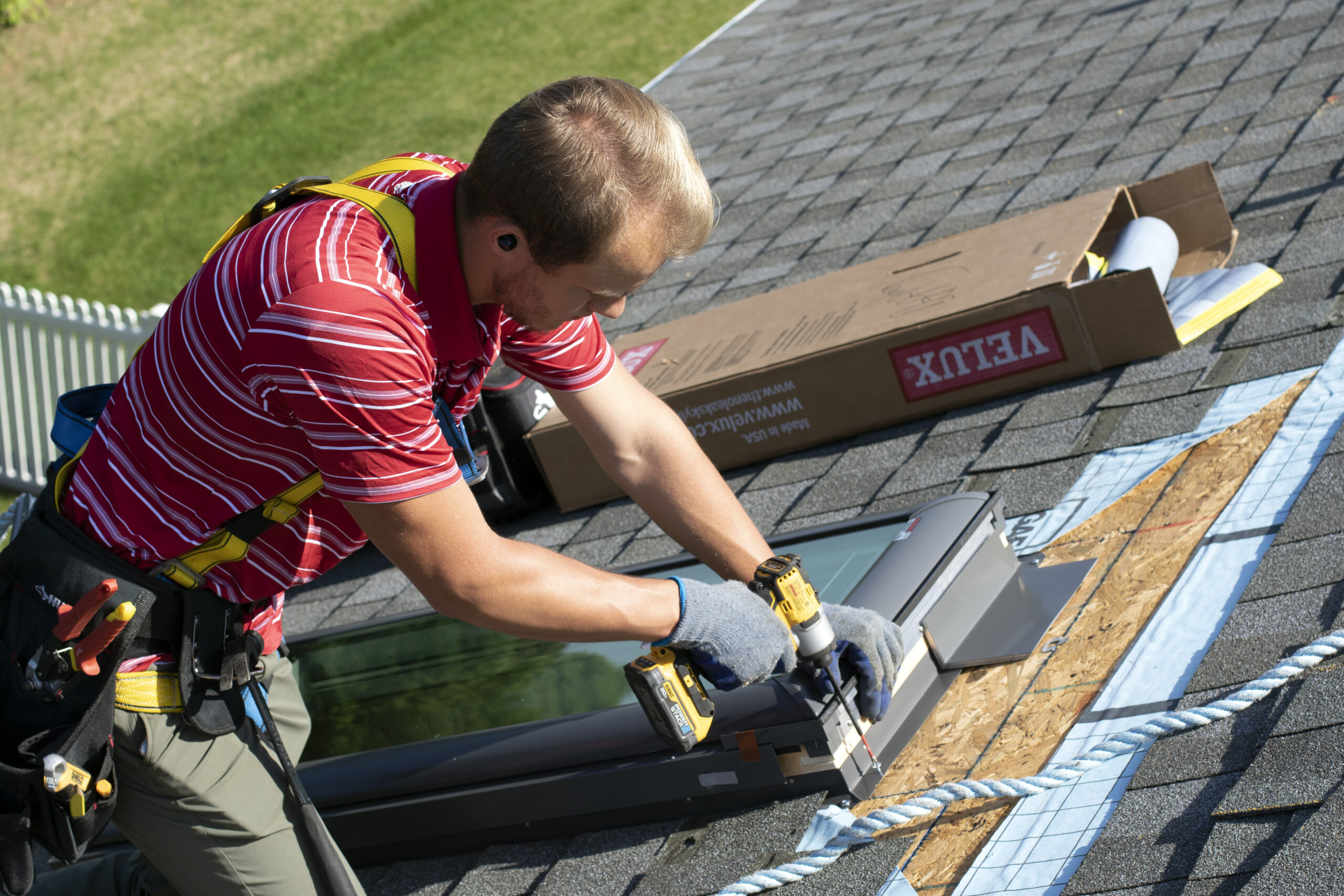 A certified professional installing a new skylight, carefully securing the frame to the roof with a drill.